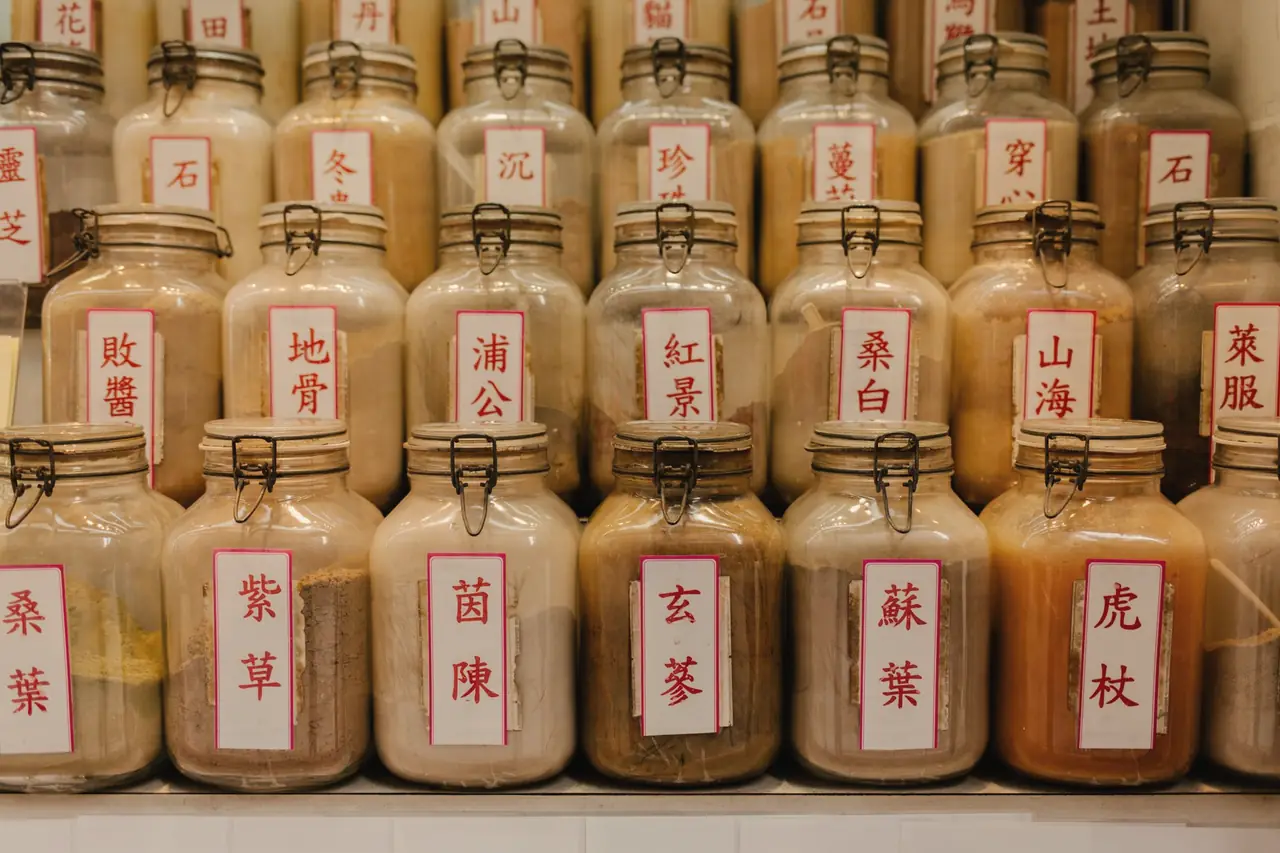 Glass jars of powdered herbs with red-bordered Chinese labels, lined up on dispensary shelves