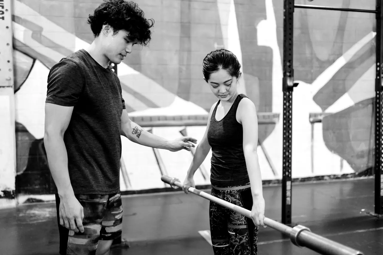 A coach shows a member where to hold the bar before her first deadlift