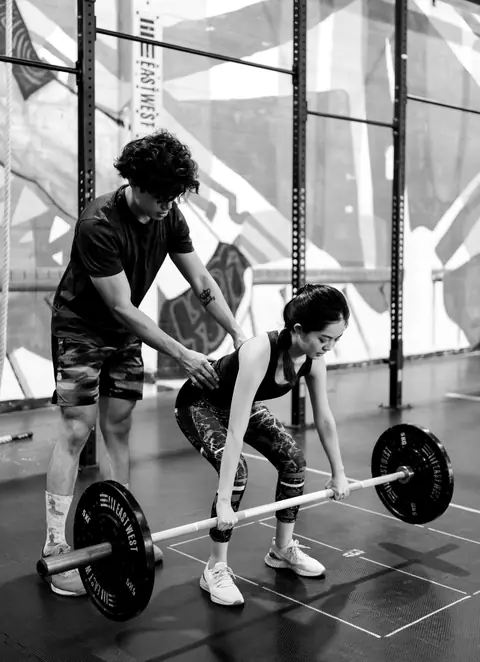 The coach checks her hip position as she sets up to pull the bar off the floor
