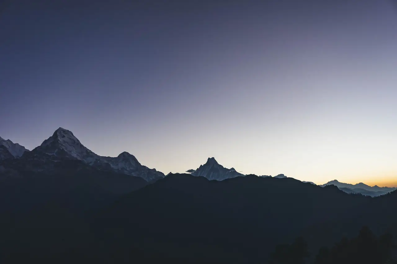 Peaks of the Annapurna range, among them the fishtail summit of Machhapuchhre, in silhouette against a violet evening sky above Pokhara