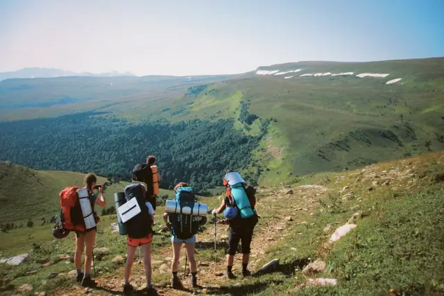 Four hikers with backpacks pausing on a grassy mountain ridge above a wide green valley