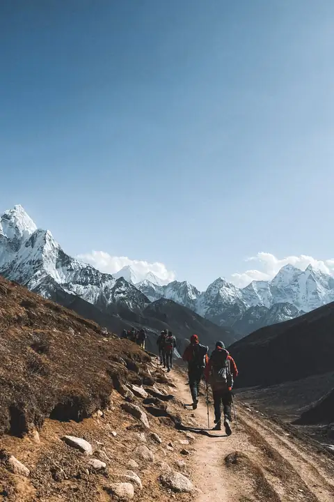 A small group of trekkers on a dusty trail below snow-capped Himalayan peaks in Nepal