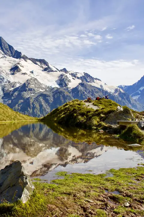 Snow-capped alpine peaks and glaciers reflected in a still mountain tarn under a blue sky