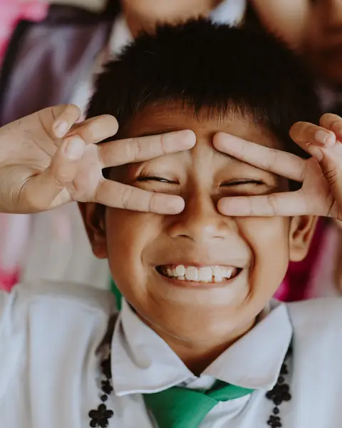 A boy in school uniform laughing, making glasses with his fingers