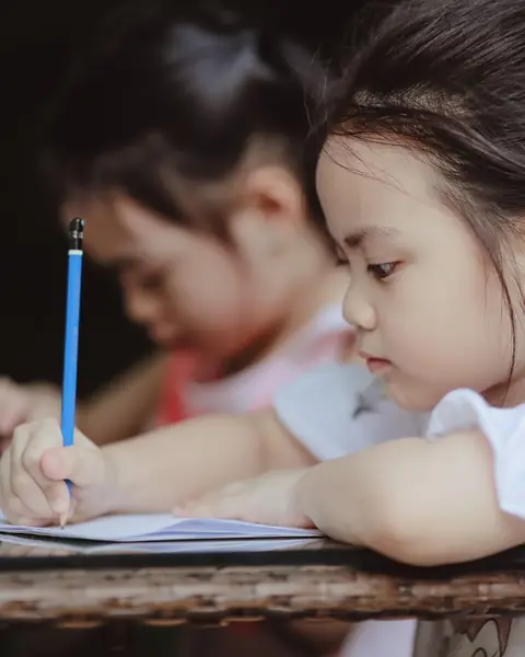 A young girl in a white dress writing carefully in her exercise book