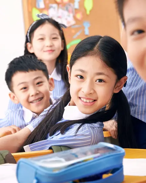 Three primary pupils in blue-striped uniforms smiling at their desks
