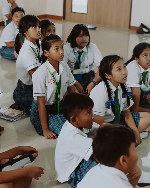 Upper primary pupils in uniform sitting on the classroom floor, looking up at the teacher
