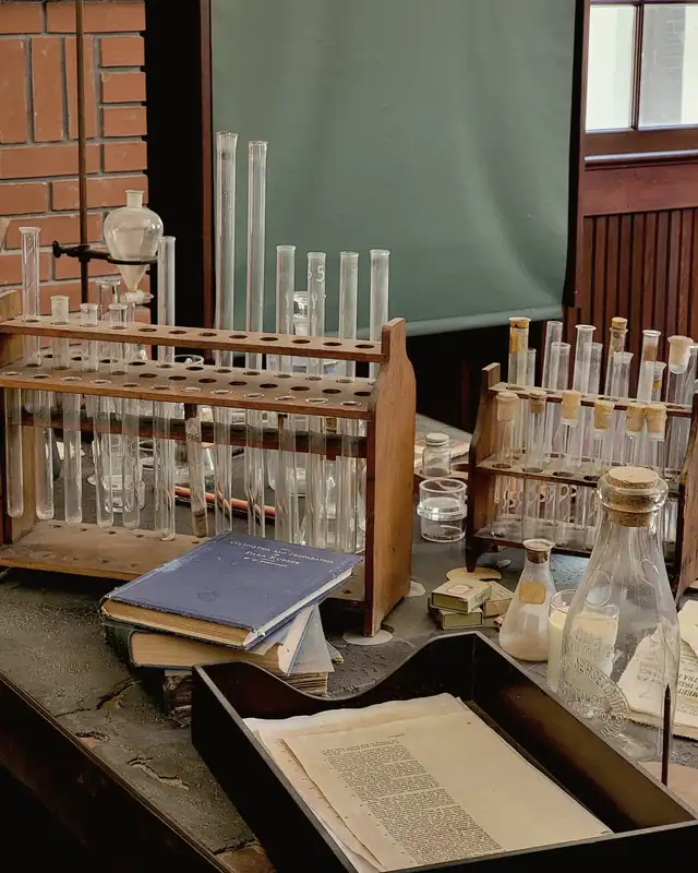 An old wooden laboratory bench with racks of glass test tubes, a flask and a stack of chemistry books