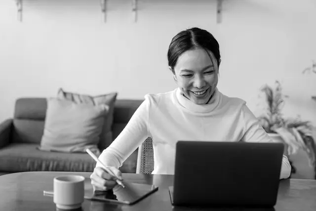 A woman smiling at her laptop on a video call at home