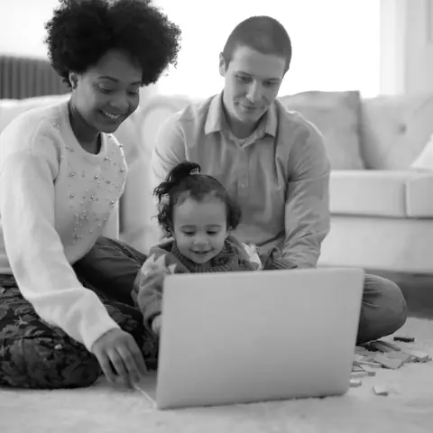 A family on the living-room floor, watching something on a laptop