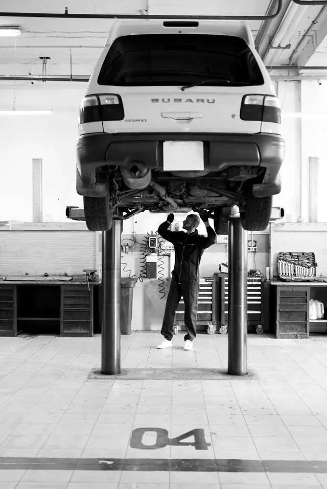 A technician under a white SUV on a two-post lift, the bay number 04 painted on the tiled floor