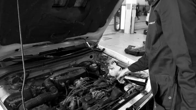 A technician in coveralls checking fluids in an open engine bay